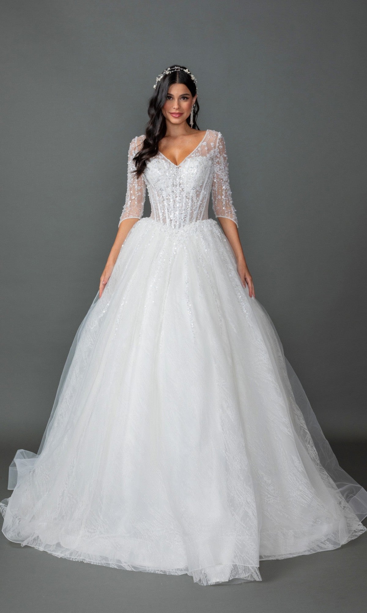 A woman wearing the Long Wedding Dress 0323 by Dancing Queen in off white, featuring a tulle ball gown silhouette with a lace-embellished bodice, sheer beaded sleeves, and a full tulle skirt, stands against a plain gray background.